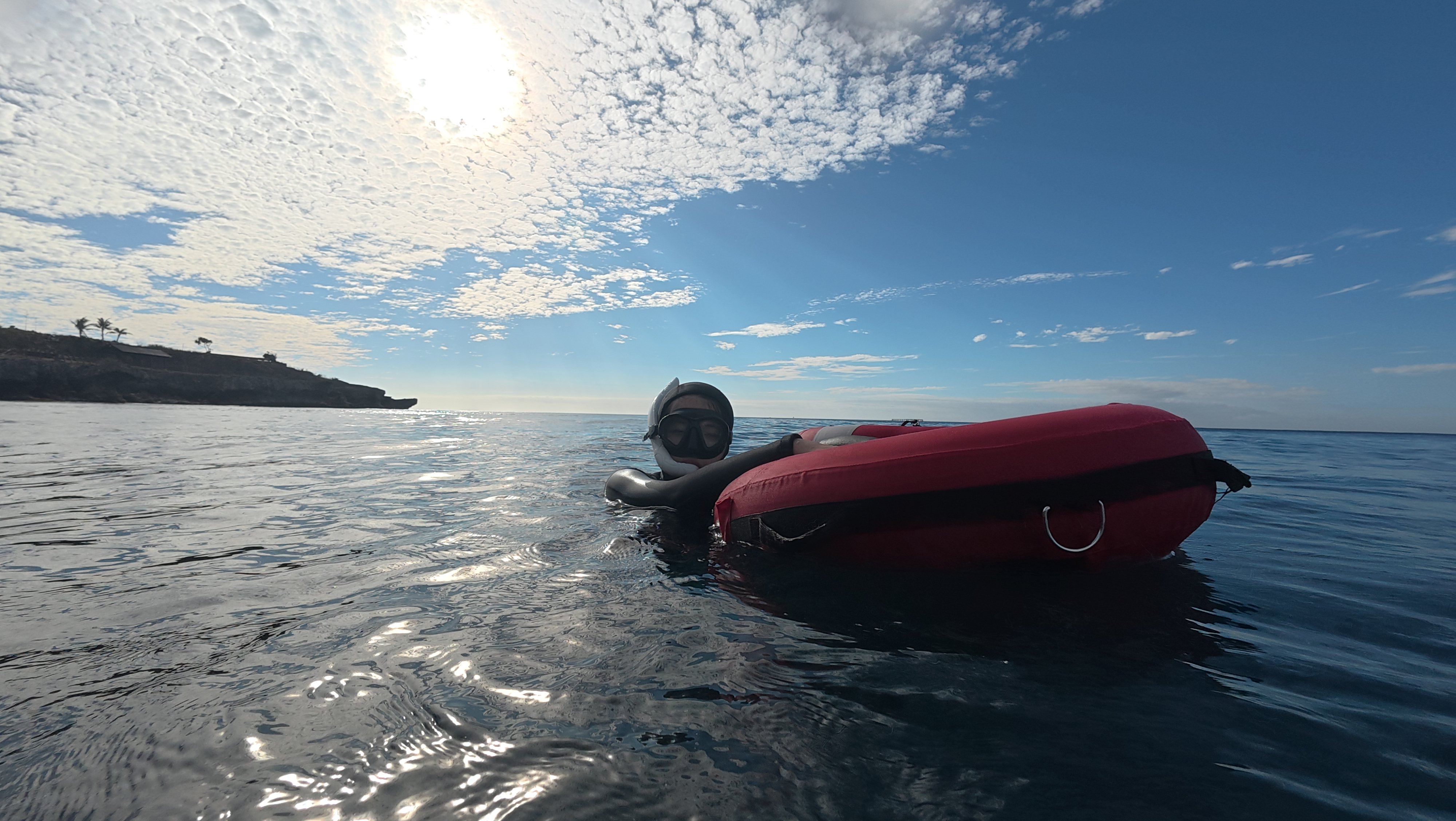 Freediver floating calmly beside a dive float, coastline in the background